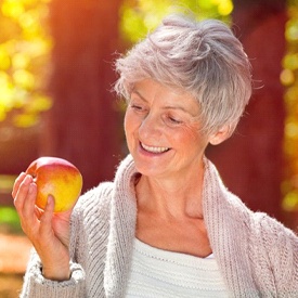Woman with dental implants in Vienna smiles at an apple