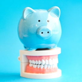 Blue piggy bank atop model of dental implants