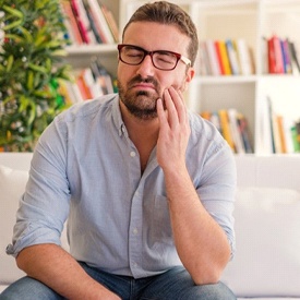 man sitting on a touch and holding his cheek in pain