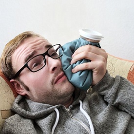 man lying on a couch and holding an ice pack to his face